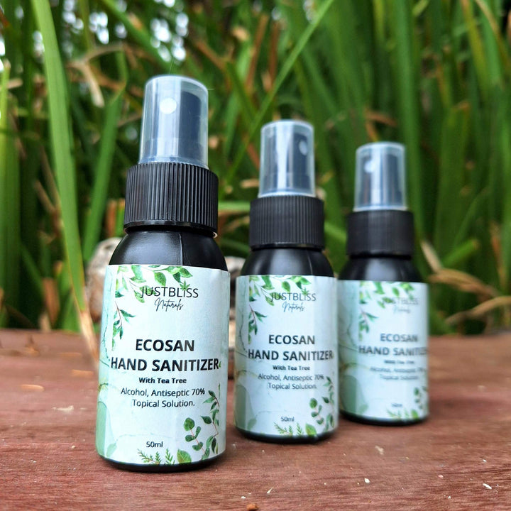 EcoSan 70% Alcohol Hand Sanitizer with Tea Tree Essential Oil bottles on wooden surface, greenery background.