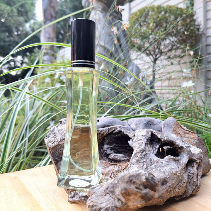 50ml oil-based floral perfume for women in an elegant bottle, set outdoors against a backdrop of greenery and rustic wood.