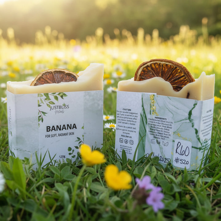 Two boxes of Just Bliss Naturals banana soap on a wooden surface with a blurred natural background.