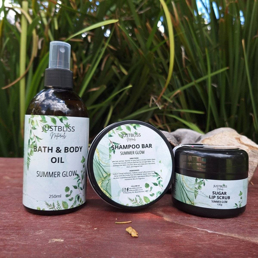 GIFT BOX: Summer Glow set with body oil, shampoo bar, and lip scrub on a wooden surface and greenery background.