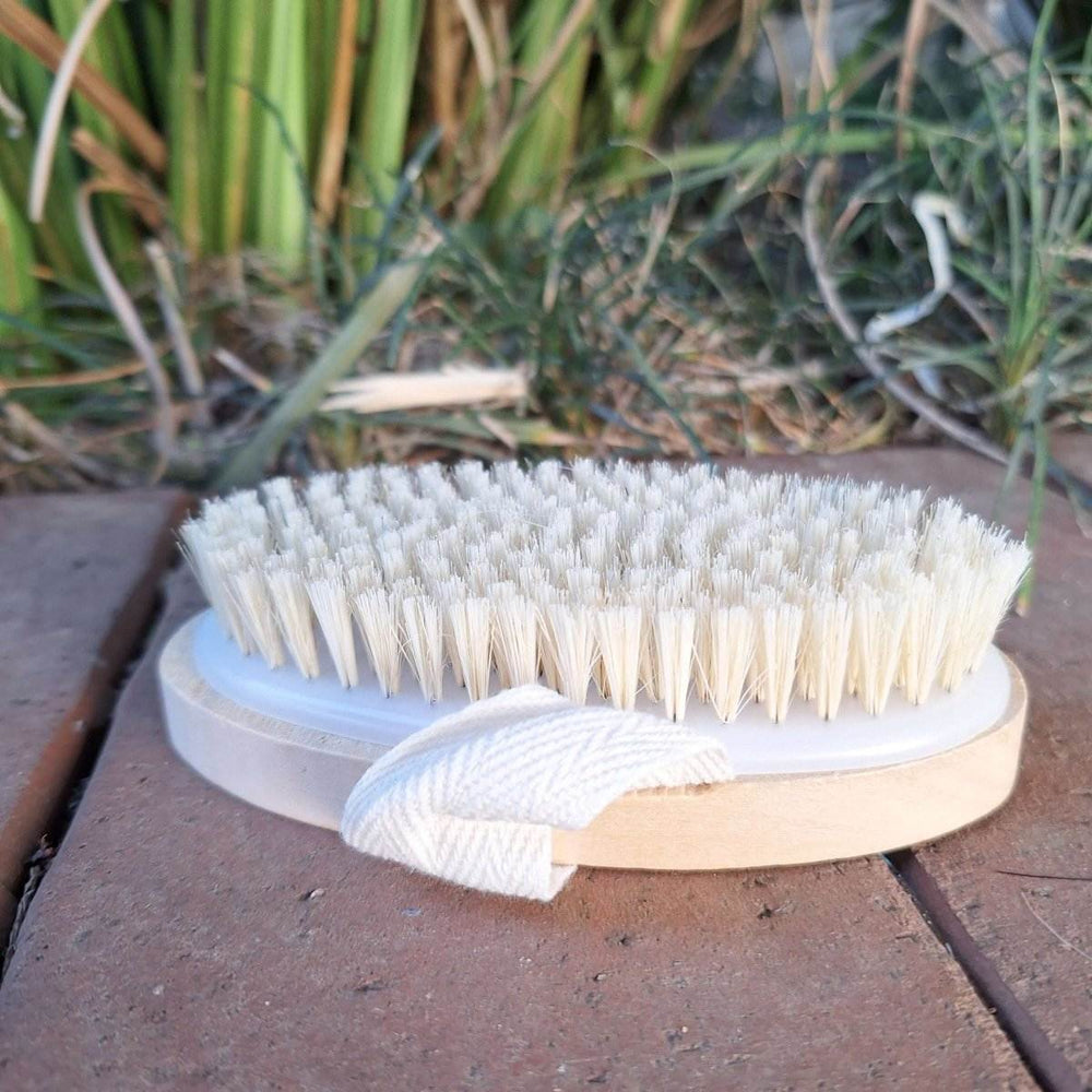 Wooden bristle body brush with ergonomic handle on a natural background.
