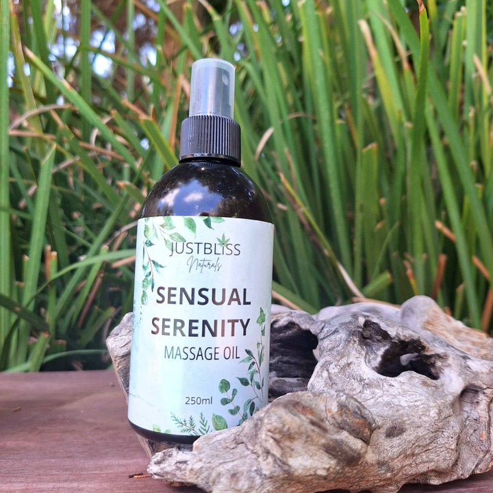 Sensual Serenity Massage Oil bottle surrounded by greenery and driftwood.