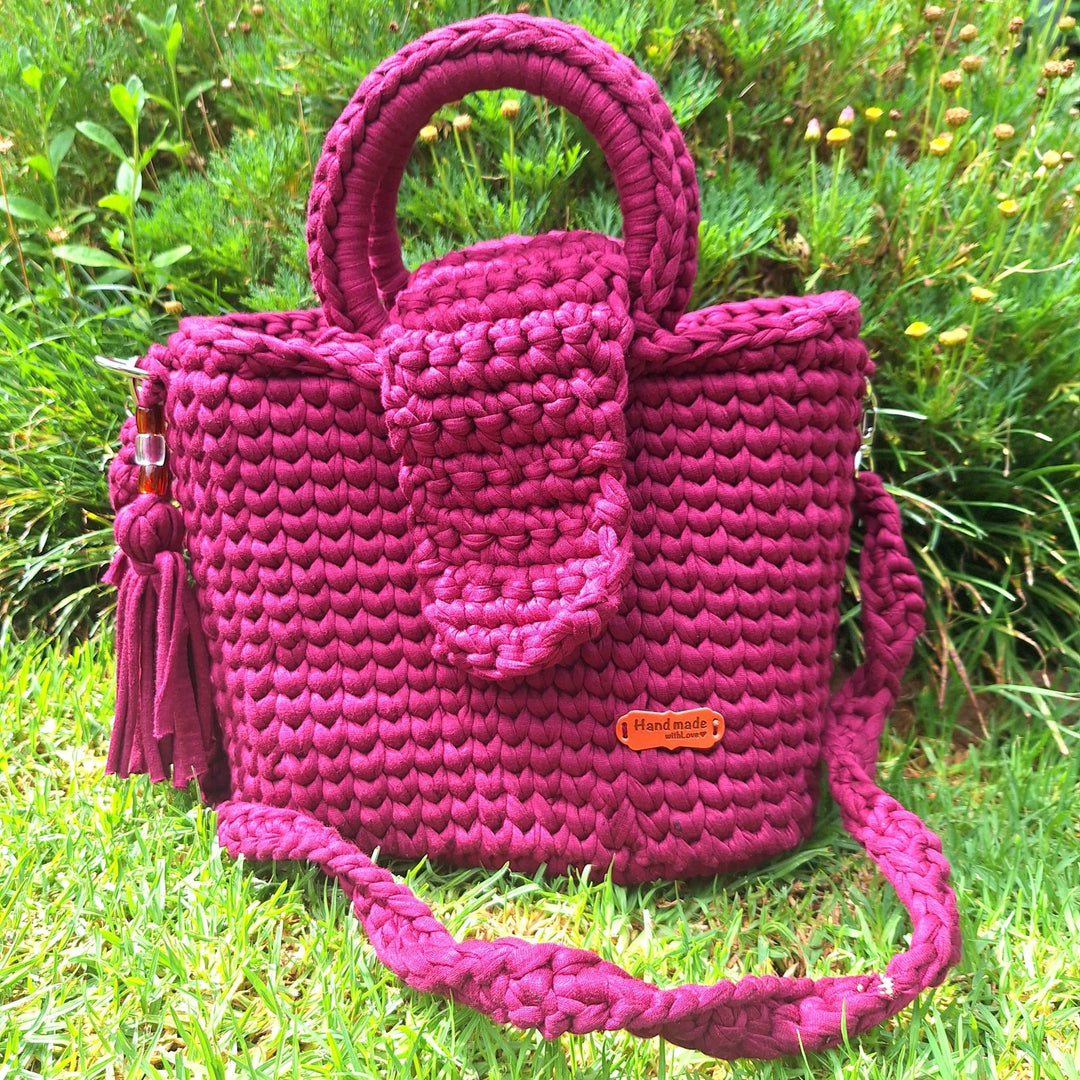 Hand-crafted handbag made with cotton wool, featuring a stitched design and tassel accents, displayed outdoors.