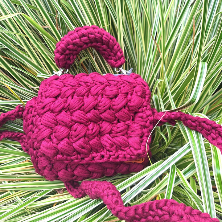 Handcrafted handbag with hand-stitched cotton wool design placed on grass.