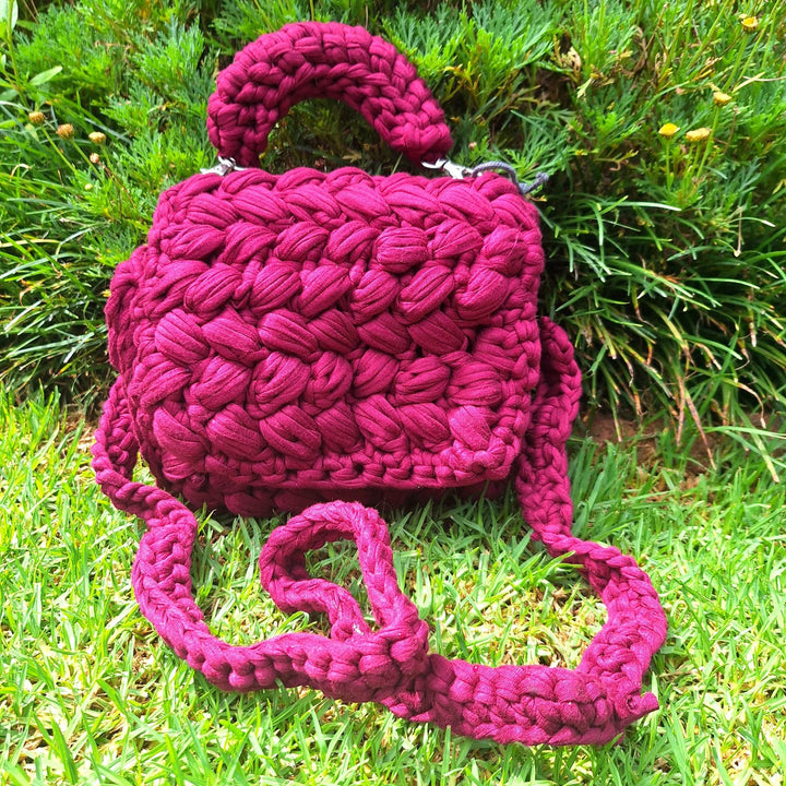 Hand-crafted handbag made with cotton wool, featuring a hand-stitched design, displayed on grass.
