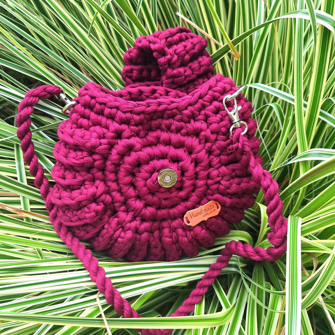Handcrafted handbag with spiral design on grass background.