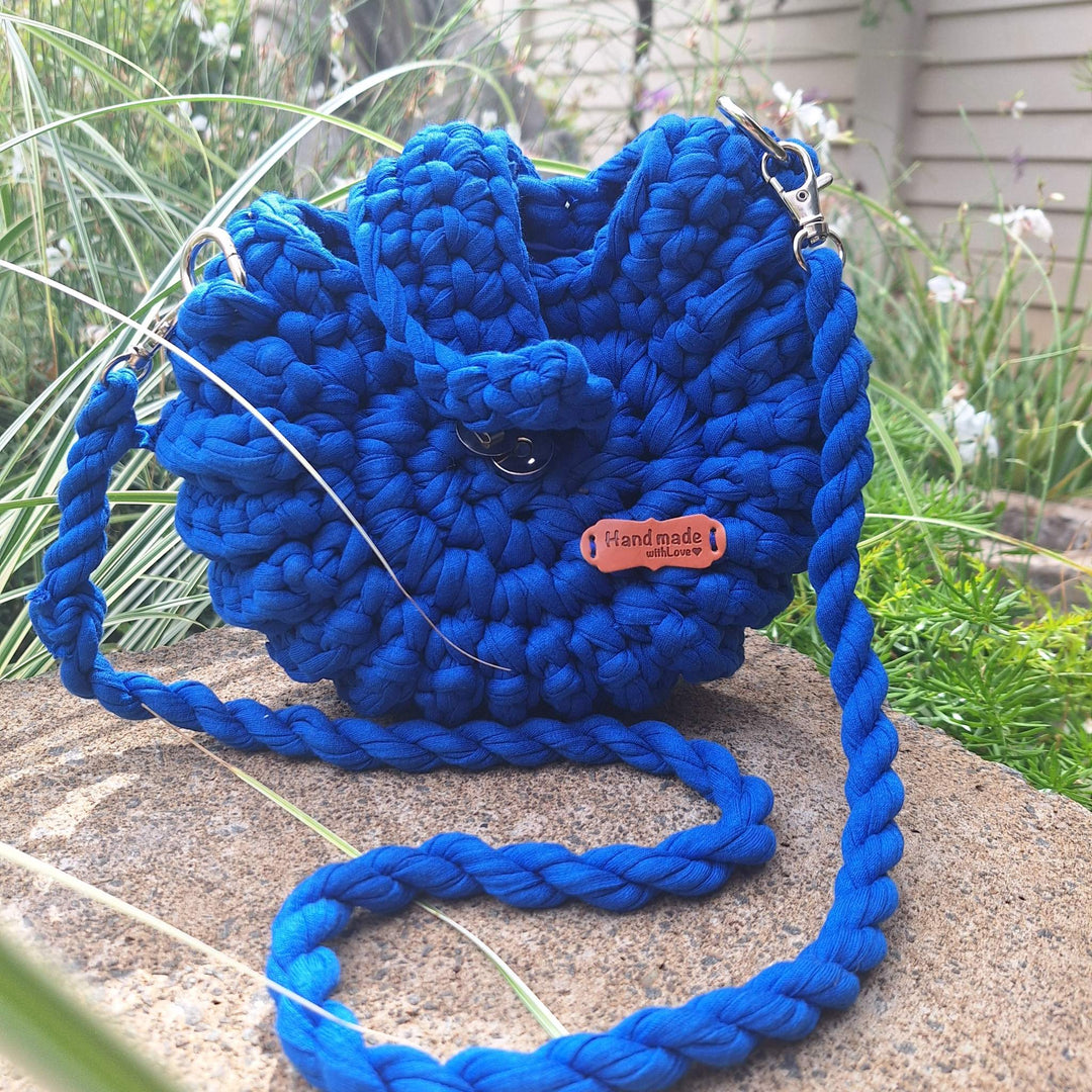 Hand-crafted handbag made with cotton wool, showcasing detailed stitching and a braided strap, set in a garden background.