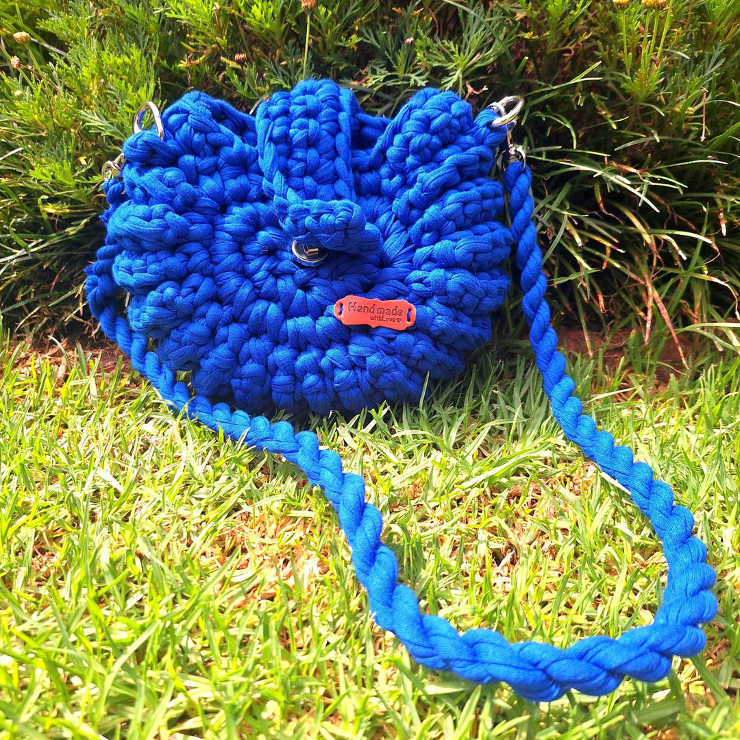 Hand-crafted handbag made of cotton wool, with a braided strap, displayed outdoors on grass.
