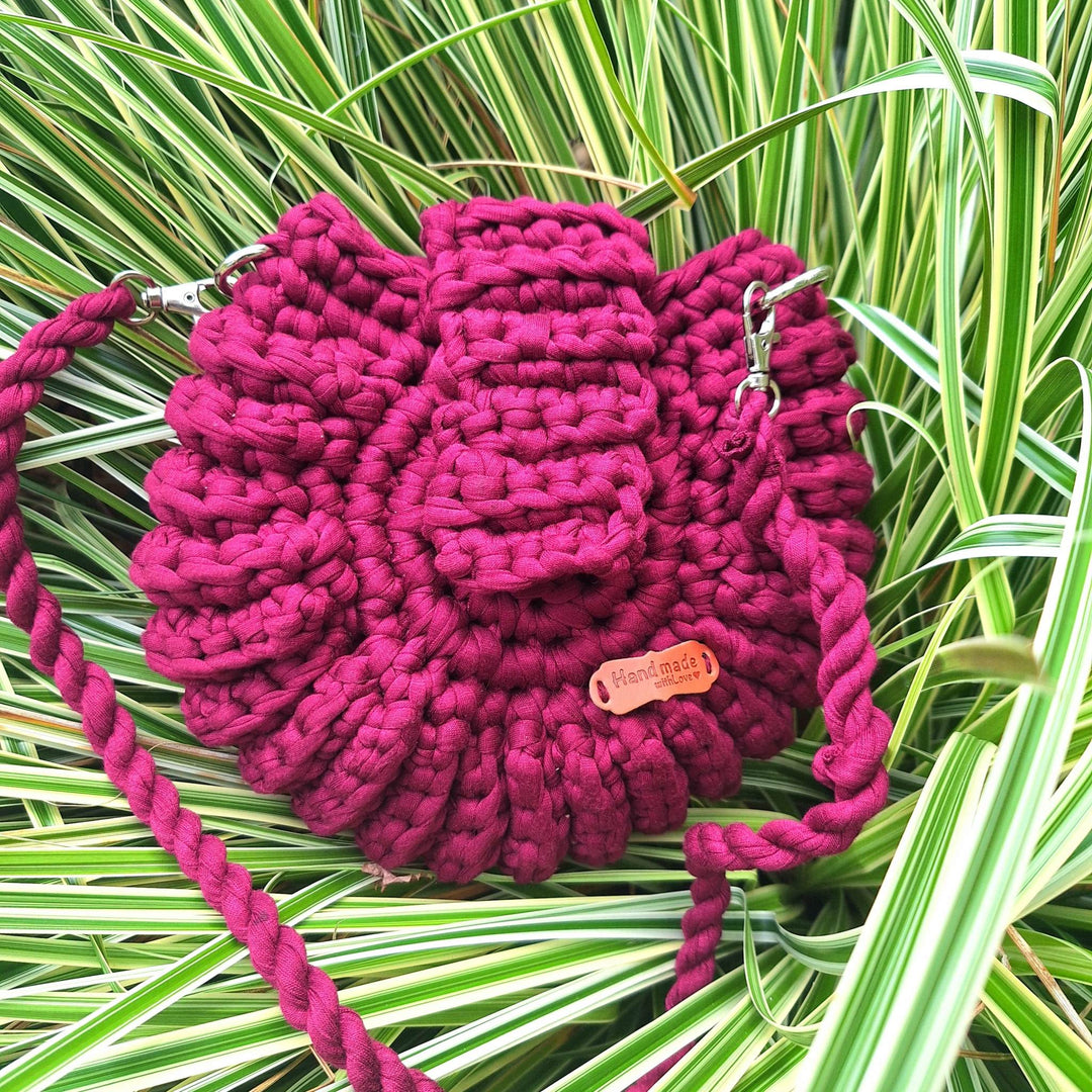 Hand-crafted handbag made from cotton wool, showcasing unique hand-stitched design against green foliage background.