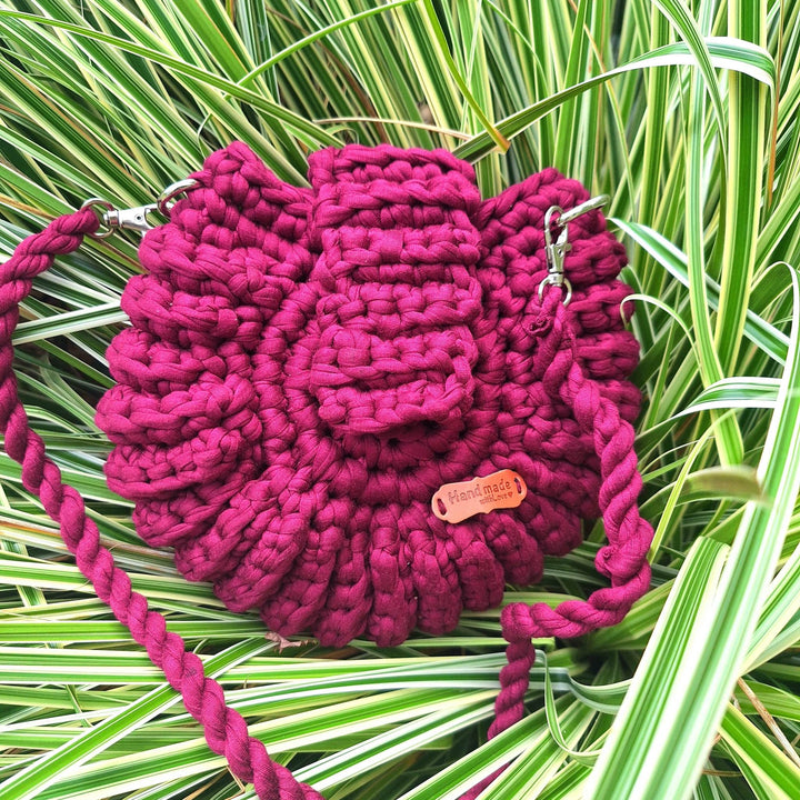 Hand-crafted handbag made from cotton wool, showcasing unique hand-stitched design against green foliage background.