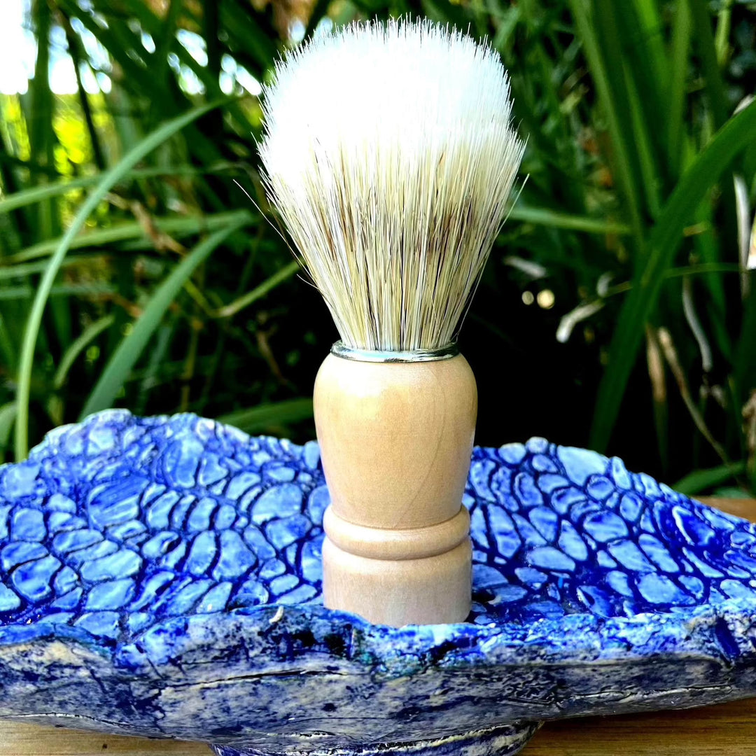 Shaving brush with natural bristles and wooden handle on blue textured dish.